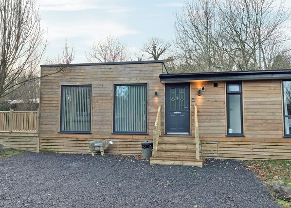 Un bâtiment moderne en bois, doté d’une porte d’entrée sombre, de deux grandes fenêtres et d’un petit porche.