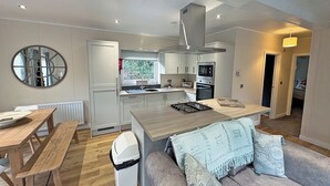 Een moderne keuken met witte kasten, een inbouwoven en een eethoek met een houten tafel en bank.
