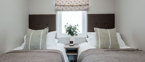 Ein Doppelzimmer mit zwei Betten, einem Fenster mit Pflanze und einem Nachttisch mit Lampe.