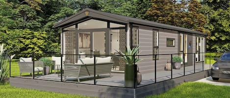 A modern mobile home with a deck, outdoor seating, and a car parked nearby.