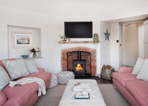 A living room with a brick fireplace, two sofas, a coffee table with books, and a television mounted above the fireplace. - 3 bedroom accommodation in Budleigh Salterton (Budleigh Salterton)