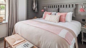 A bedroom with a bed, a bedside table, a window with curtains, and a wall-mounted towel rack. - 3 bedroom accommodation in Budleigh Salterton (Budleigh Salterton)