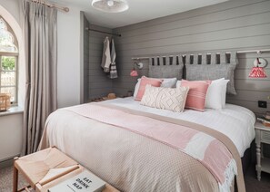 A bedroom with a bed, a bedside table, a window with curtains, and a wall-mounted towel rack. - 3 bedroom accommodation in Budleigh Salterton (Budleigh Salterton)