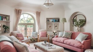 A cozy living room with a pink sofa, a matching armchair, a coffee table, and a bookshelf. - 3 bedroom accommodation in Budleigh Salterton (Budleigh Salterton)