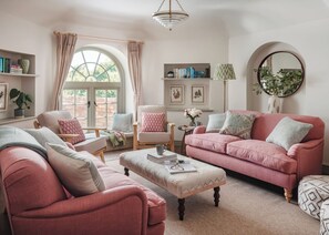 A cozy living room with a pink sofa, a matching armchair, a coffee table, and a bookshelf. - 3 bedroom accommodation in Budleigh Salterton (Budleigh Salterton)