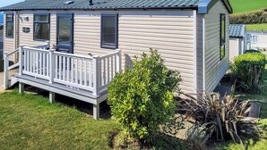 A mobile home with a porch, a chimney, and a small garden. - This comfortable stylish caravan offers beautiful sea and country views. (Dorchester)