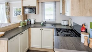 A compact kitchen with a microwave, toaster, sink, and stove. - This comfortable stylish caravan offers beautiful sea and country views. (Dorchester)