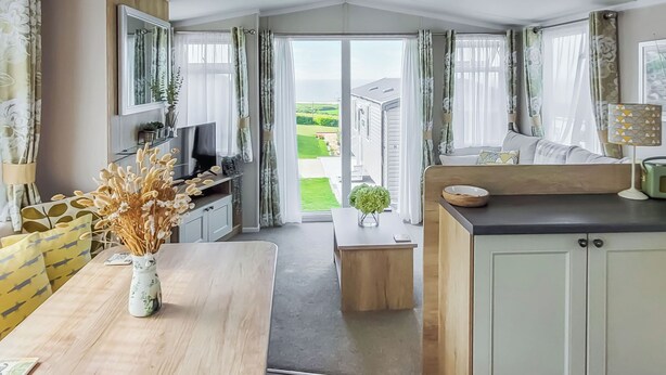 A modern kitchen with a dining area, a TV, and a view of the outdoors. - This comfortable stylish caravan offers beautiful sea and country views. (Dorchester)