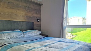 Een slaapkamer met een bed, houten hoofdeinde en een raam met uitzicht op een huis en gazon.