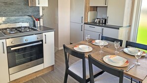 Een compacte keuken met een gasfornuis, oven en moderne kastjes. Een eettafel met borden en glazen is gedekt voor twee personen.