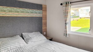 A bed with striped bedding, a grey headboard, a small bedside table, and a window with curtains. - 2 bedroom accommodation in Dorchester (Dorchester)