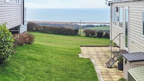A residential property with a well-maintained lawn, a stone pathway, and a view of the sea. - This comfortable stylish caravan offers beautiful sea and country views. (Dorchester)