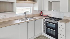 A modern kitchen with white cabinets, a stainless steel sink, a gas stove, and a built-in oven. - This comfortable stylish caravan offers beautiful sea and country views. (Dorchester)