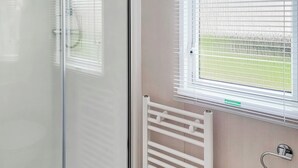 A room with a sliding glass door, a radiator, and a window with blinds. - This comfortable stylish caravan offers beautiful sea and country views. (Dorchester)