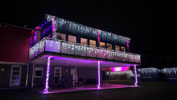 Ein zweistöckiges Gebäude mit einem Balkon und einer überdachten Terrasse, beide mit Lichterketten geschmückt.