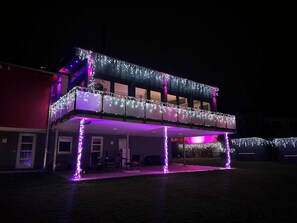 Un bâtiment à deux étages doté d’un balcon et d’un patio couvert, tous deux décorés de guirlandes lumineuses.