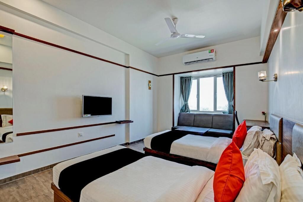 A hotel room with two beds, a television, an air conditioning unit, and a window with curtains.