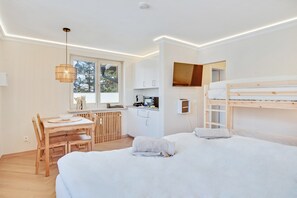 A modern room with a bunk bed, a dining table with chairs, a kitchen area, and a window with a view of trees. - Apartment "Home by the Spa Gardens" with Mountain View and Wi-Fi (Bad Reichenhall)