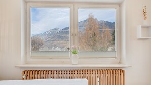 Ein Schlafzimmer mit einem großen Fenster, einer Heizung und einem Nachttisch mit einer Vase.