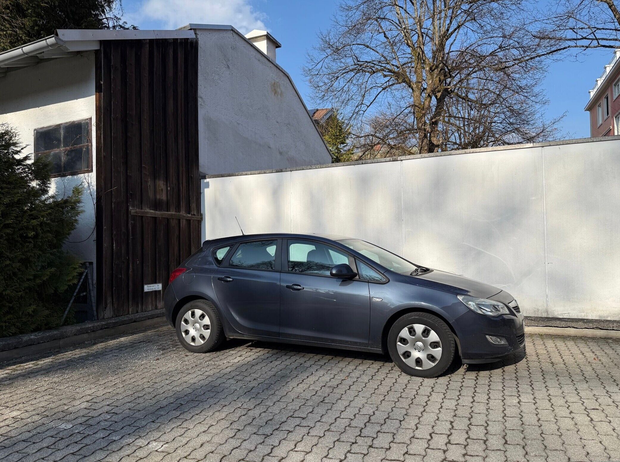 Un coche pequeño aparcado frente a un edificio con una verja de metal y un muro de hormigón.