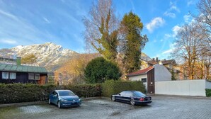 Ein Parkplatz mit zwei Autos, ein Berg im Hintergrund und ein Gebäude mit rotem Dach.
