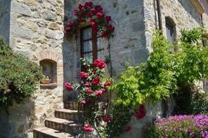A stone building with a window adorned with red flowers, a staircase, and surrounding greenery. - Lia Holiday Home, Private Pool and View (Seggiano)