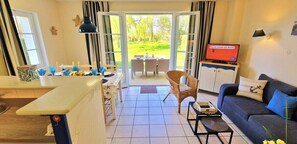 Een kamer met een eettafel, een bank, een televisie en uitzicht op het omliggende landschap.