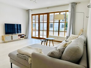 A modern living room with a sofa, a TV, a small table, and large windows.