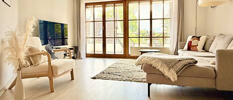 A living room with a sofa, armchair, TV, and large windows.