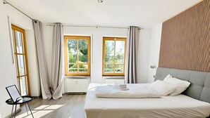 Een slaapkamer met een bed, twee ramen, een radiator en een stoel.