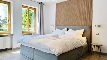 A modern bedroom with a large bed, a wooden panel wall, and a view of greenery outside.