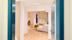 Ein Innenraum einer modernen Wohnung mit Holzboden, einem weißen Sofa und einem Essbereich mit Tisch und Stühlen.