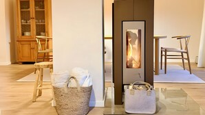 Ein modernes Interieur mit Kaminofen, Holzschrank, Esstisch mit Stühlen und einem gewebten Korb.