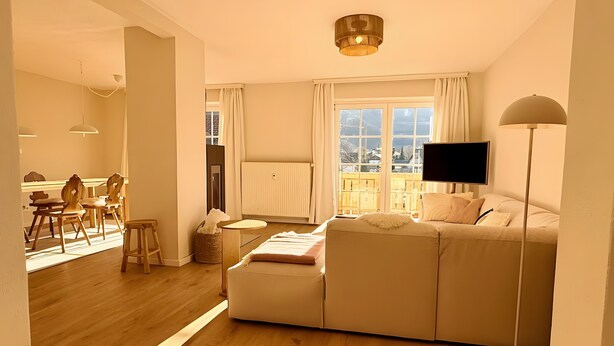 Ein modernes Wohnzimmer mit einer Couch, einem Fernseher, einer Stehlampe und einem Essbereich mit Stühlen und einem Tisch.