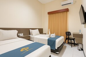 Habitación de hotel con dos camas, un escritorio, una silla, un equipo de aire acondicionado y un televisor.
