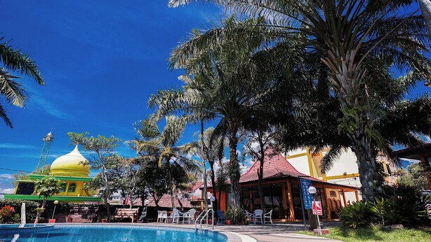 A pool area with a yellow dome structure, palm trees, and a building with a red roof. - Tripletree Ciptaningati Culture Hotel (Batu)