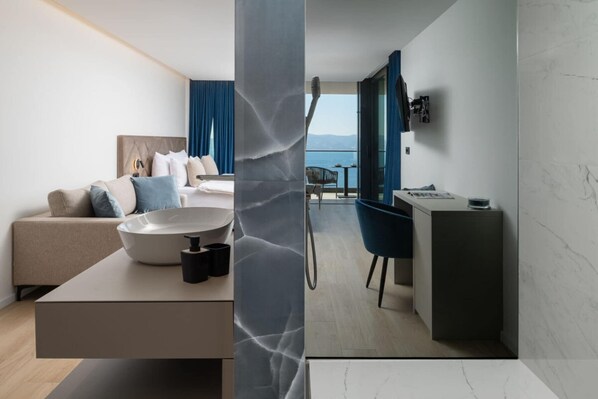 A modern hotel room with a minimalist design, featuring a sofa, a dining area with a table and chairs, and a view of the sea through large windows. - Luxury Villa Hedonia (Brela)
