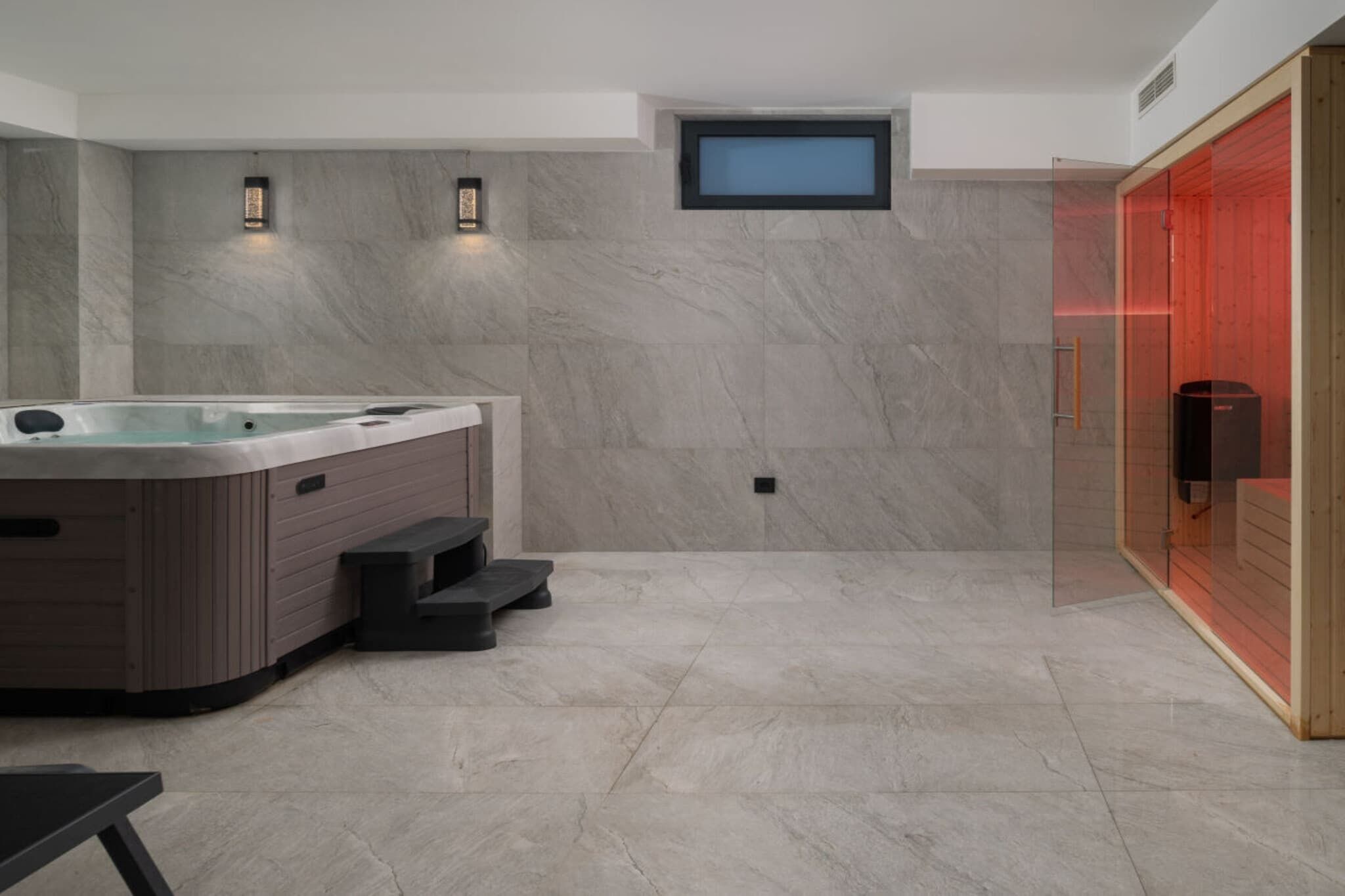 A modern bathroom with a marble wall, a hot tub, and a glass-enclosed shower area.