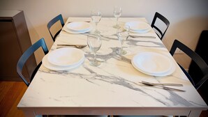 Una mesa de comedor con cubierta de mármol, cuatro platos blancos, tres copas de vino y cubiertos.