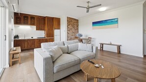 Un salon moderne avec un canapé d’angle gris, une table basse en bois et un coin repas comprenant une petite table et un banc.