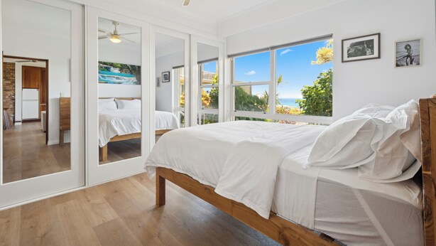 Une chambre dotée d’un grand lit, d’un ventilateur de plafond et offrant une vue sur l’extérieur grâce à de grandes fenêtres.