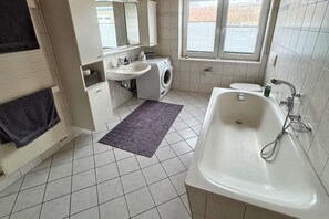 A bathroom with a sink, washing machine, toilet, and bathtub.