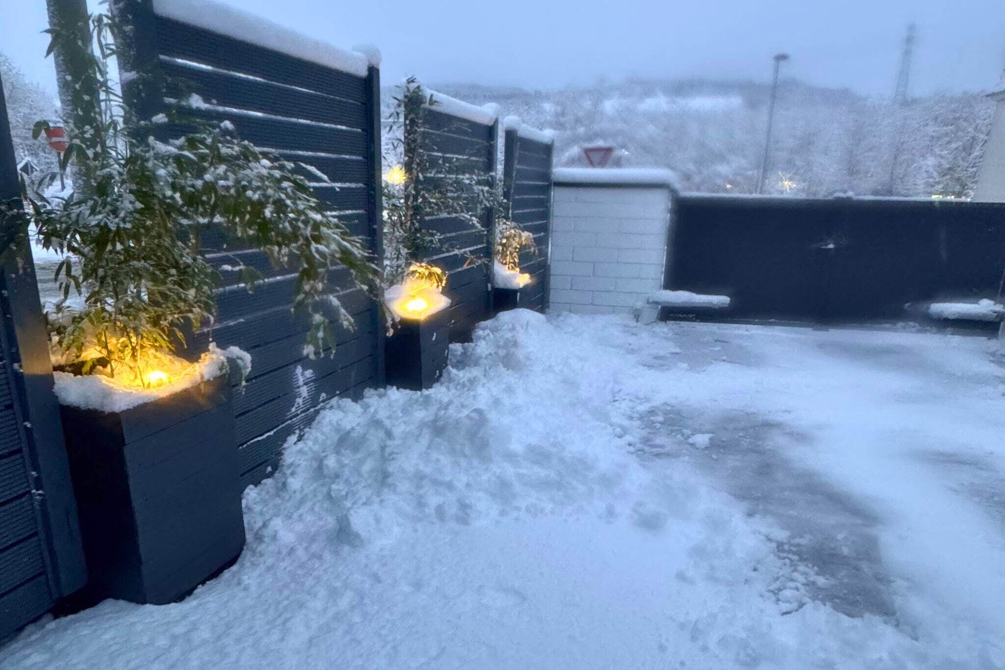 A snow-covered outdoor area with a wooden fence, a brick wall, and a gate.