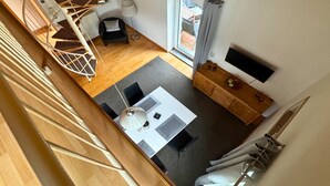 A spacious room with a wooden staircase, a dining area with a table and chairs, a small seating area, and a window with a view of the outside.