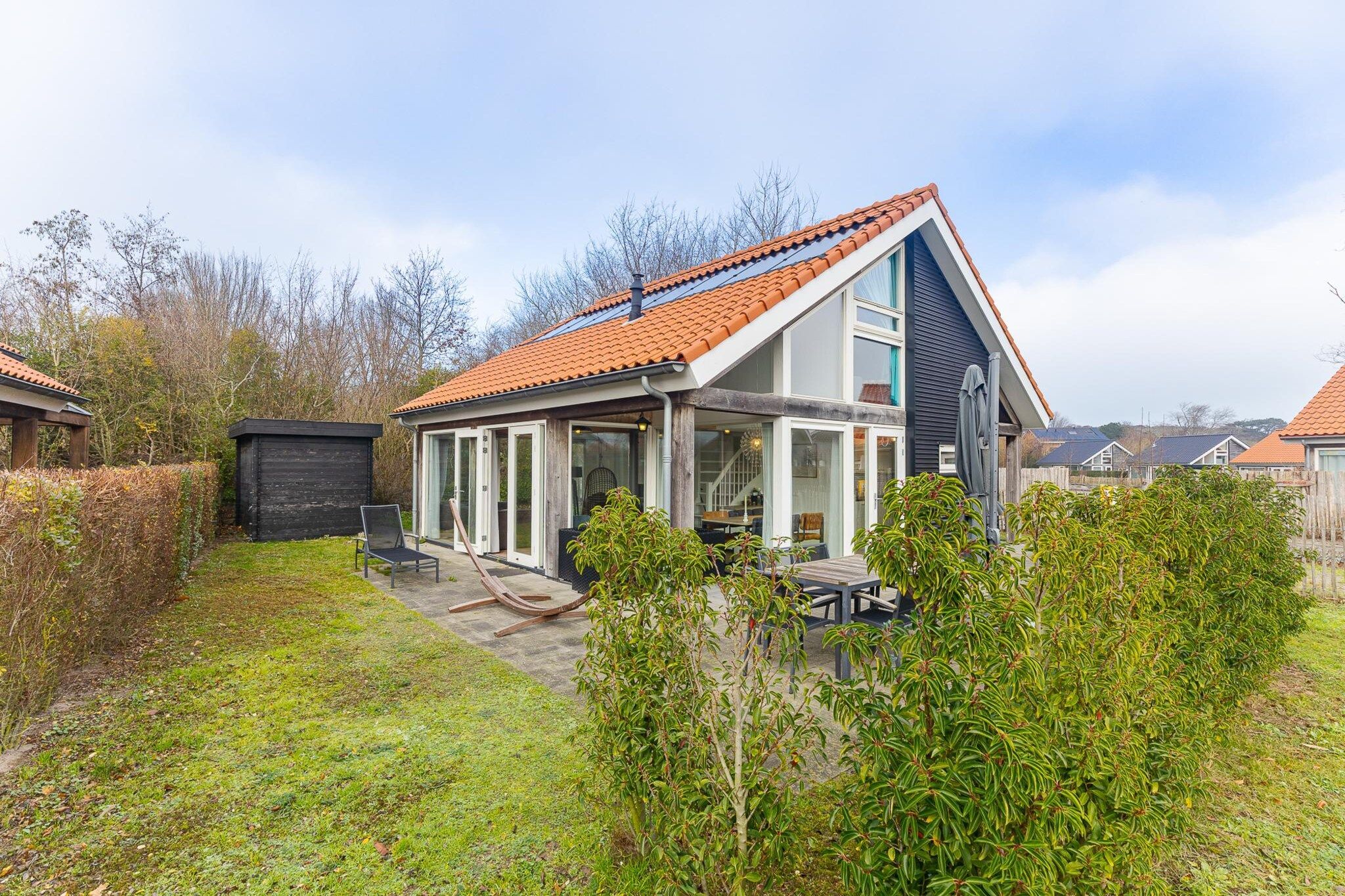 A modern house with a sloped roof, large windows, and a covered patio area.