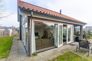 A house with a covered patio, sliding glass doors, and a tiled roof. - Coastal Family Escape with Enclosed Garden (Renesse)