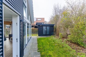 A modern house with a glass door entrance, a small outdoor seating area, and a garden with a shed. - Coastal Family Escape with Enclosed Garden (Renesse)