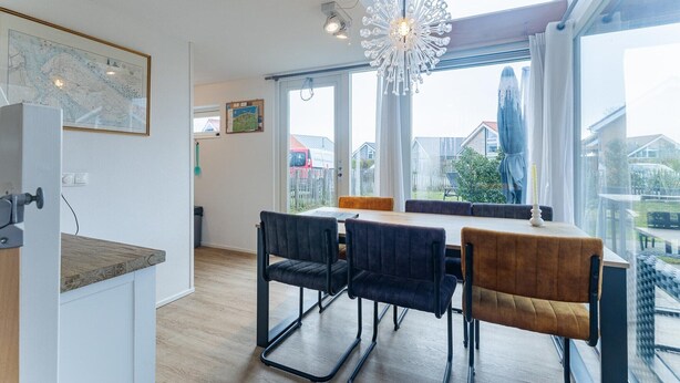 A modern dining area with a table and chairs, large windows, and a map on the wall. - Coastal Family Escape with Enclosed Garden (Renesse)