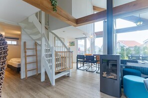 Amplia sala de estar con una escalera de madera, una mesa de comedor con sillas y un gran ventanal con vistas al exterior.