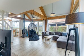 Amplia sala de estar con techo de madera, una silla colgante, un sofá y un televisor.